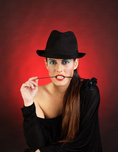 Mujer con sombrero negro posando sobre un fondo rojo en un retrato de estudio