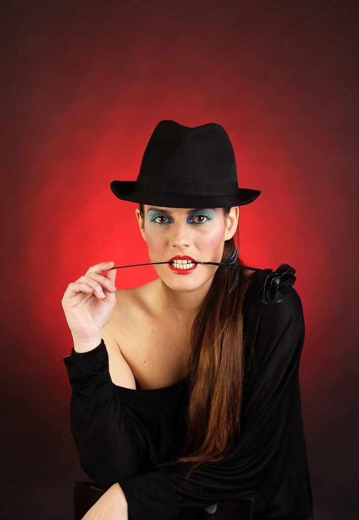 Mujer con sombrero negro posando sobre un fondo rojo en un retrato de estudio