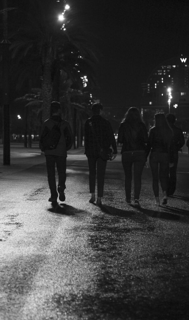 Grupo de personas caminando de espaldas por un paseo nocturno de la Barceloneta, en blanco y negro