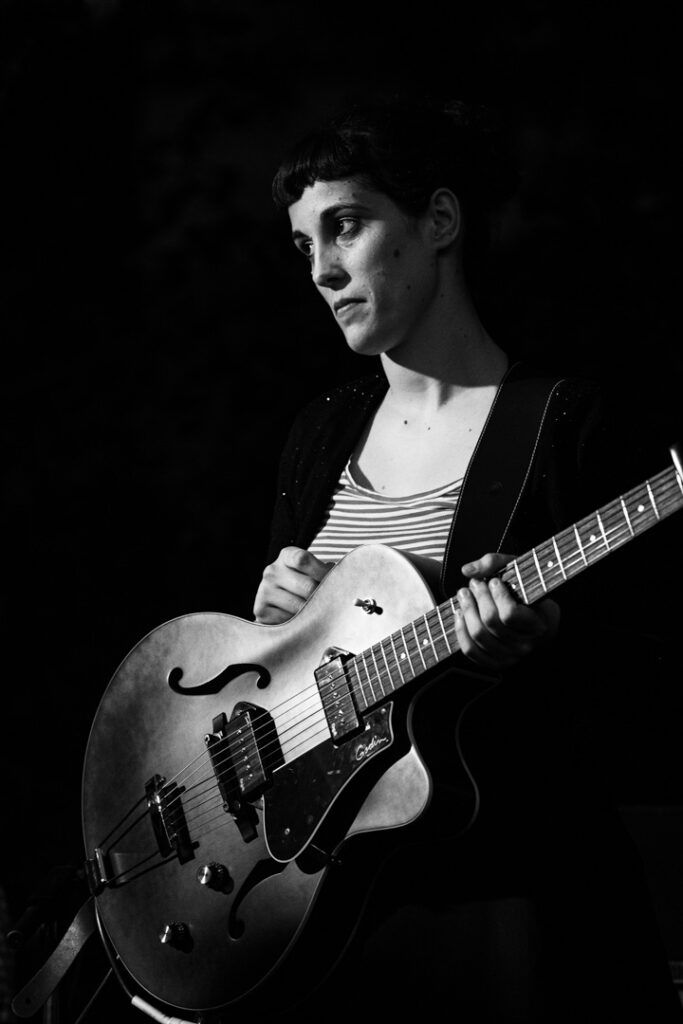 Guitarrista tocando una guitarra eléctrica apoyada sobre el regazo en directo, blanco y negro