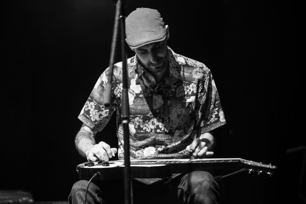 Músico tocando una guitarra lap steel sentado, con gorra, fotografía en blanco y negro