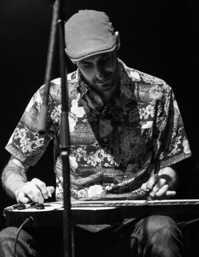 Músico tocando una guitarra lap steel sentado, con gorra, fotografía en blanco y negro