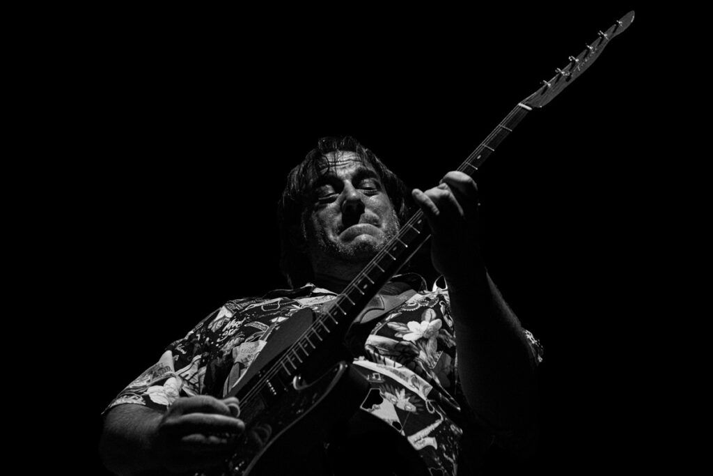 Guitarrista con camisa estampada tocando la guitarra eléctrica en directo, blanco y negro