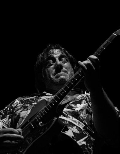 Guitarrista con camisa estampada tocando la guitarra eléctrica en directo, blanco y negro