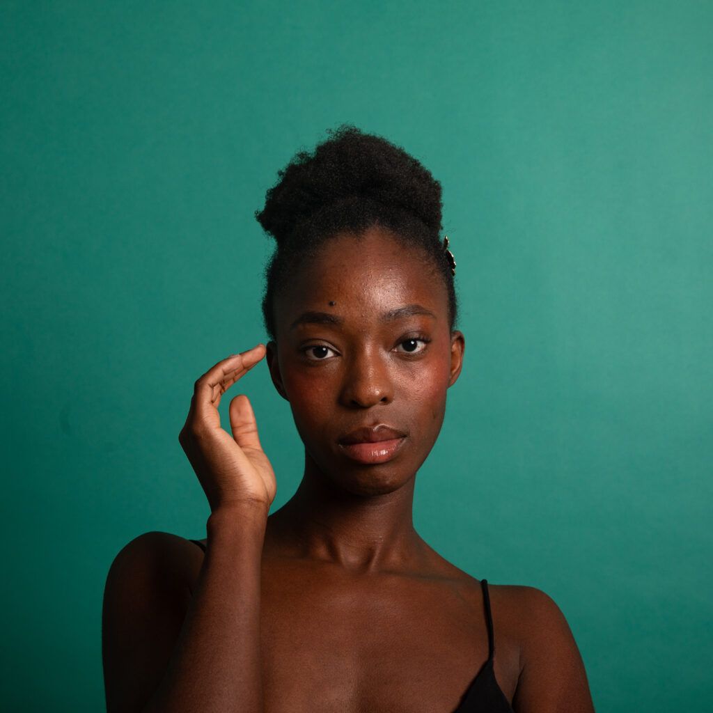 Retrato de estudio de una mujer con la mano junto al rostro sobre fondo verde