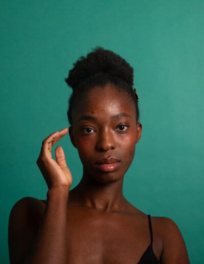 Retrato de estudio de una mujer con la mano junto al rostro sobre fondo verde