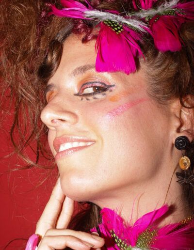 Mujer con cabello rizado, maquillaje artístico y plumas de color magenta en un retrato de moda