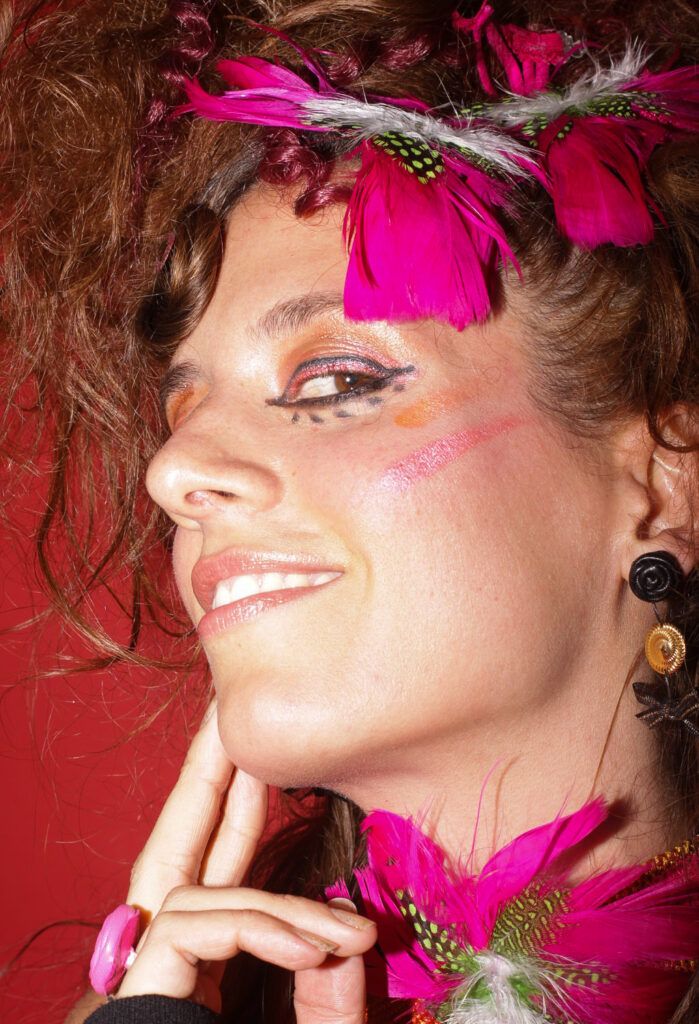 Mujer con cabello rizado, maquillaje artístico y plumas de color magenta en un retrato de moda