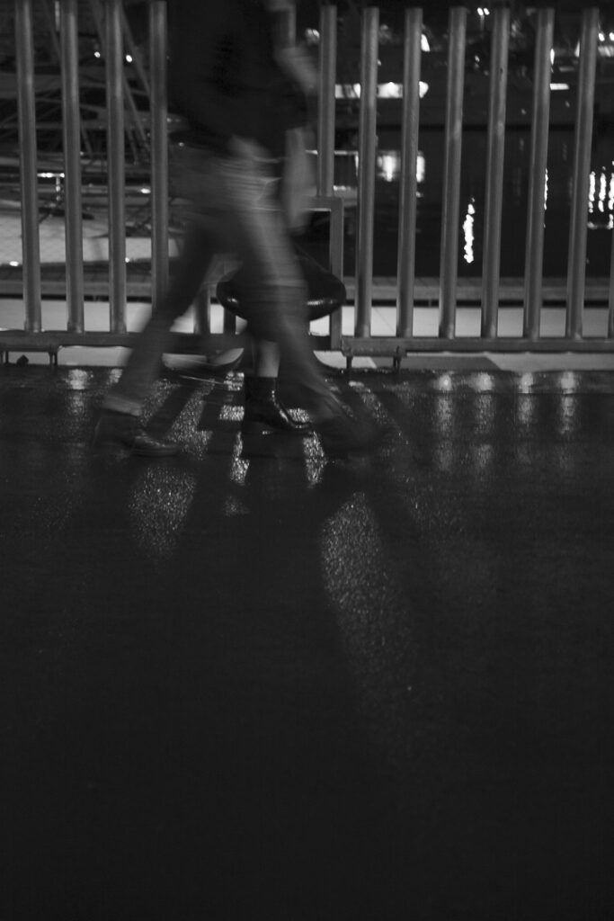 Persona caminando de noche junto a una verja en la Barceloneta, en blanco y negro