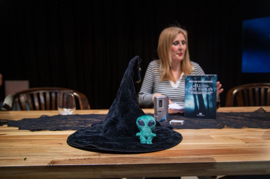 Presentadora del podcast sentada a la mesa junto a un sombrero de bruja