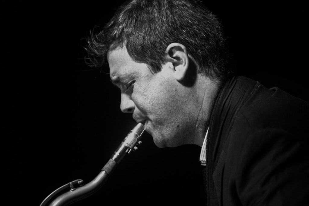 Saxofonista de jazz de perfil tocando el saxo en directo, fotografía en blanco y negro