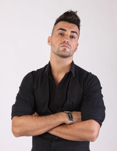 Retrato de estudio de un hombre joven con camisa negra y los brazos cruzados sobre fondo claro