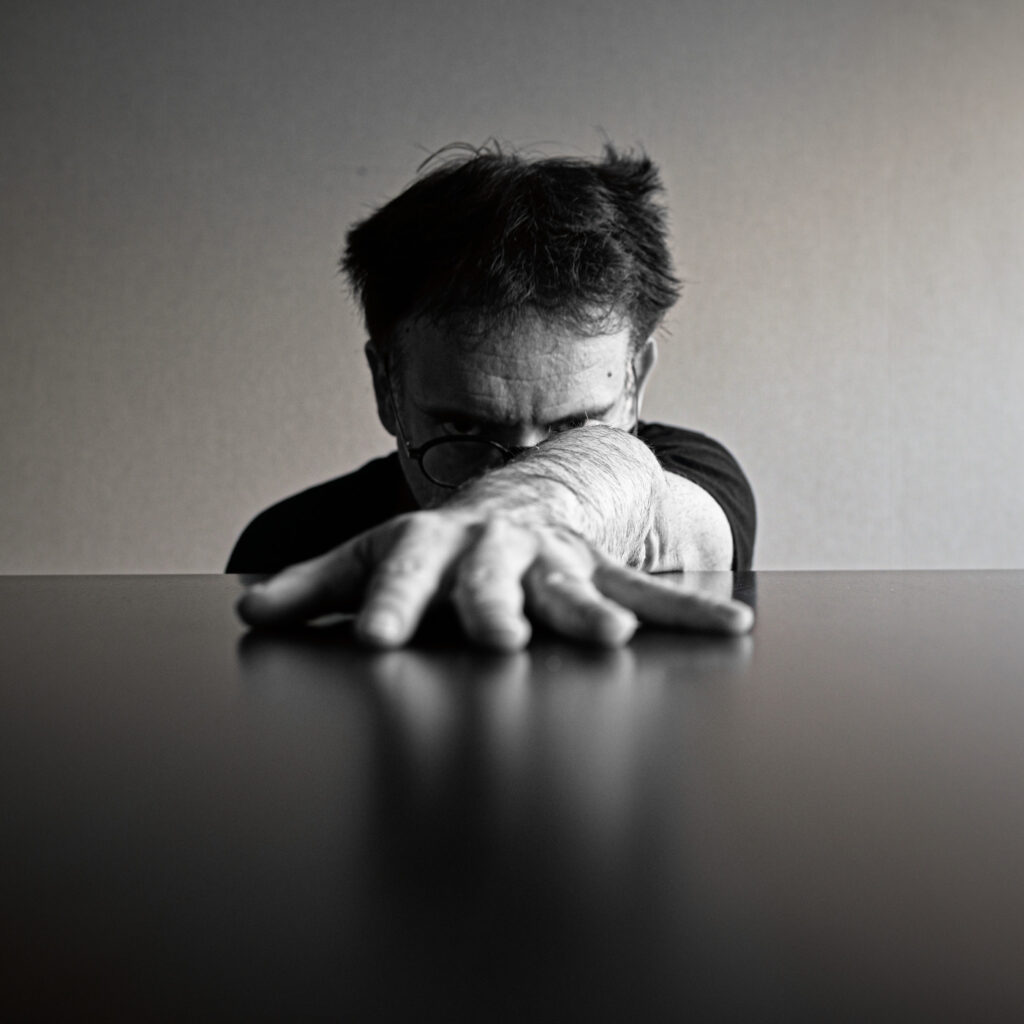 Autorretrato en blanco y negro con la cara medio oculta detrás de la mano, apoyado en una mesa