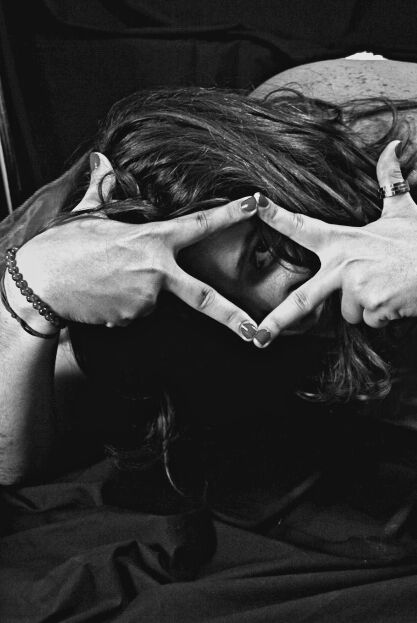 Retrato en blanco y negro de una mujer que enmarca su ojo con las manos entre el pelo