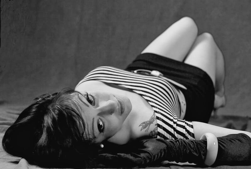 Retrato en blanco y negro de una mujer tumbada con camiseta de rayas mirando a cámara