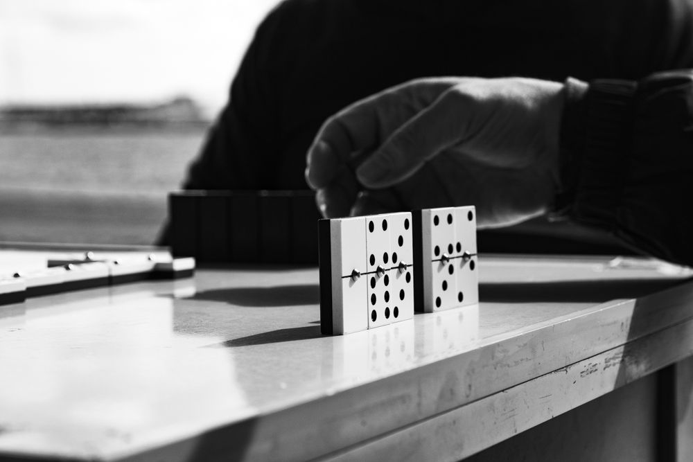 Mano sujetando dos fichas de dominó al borde de la mesa, en blanco y negro