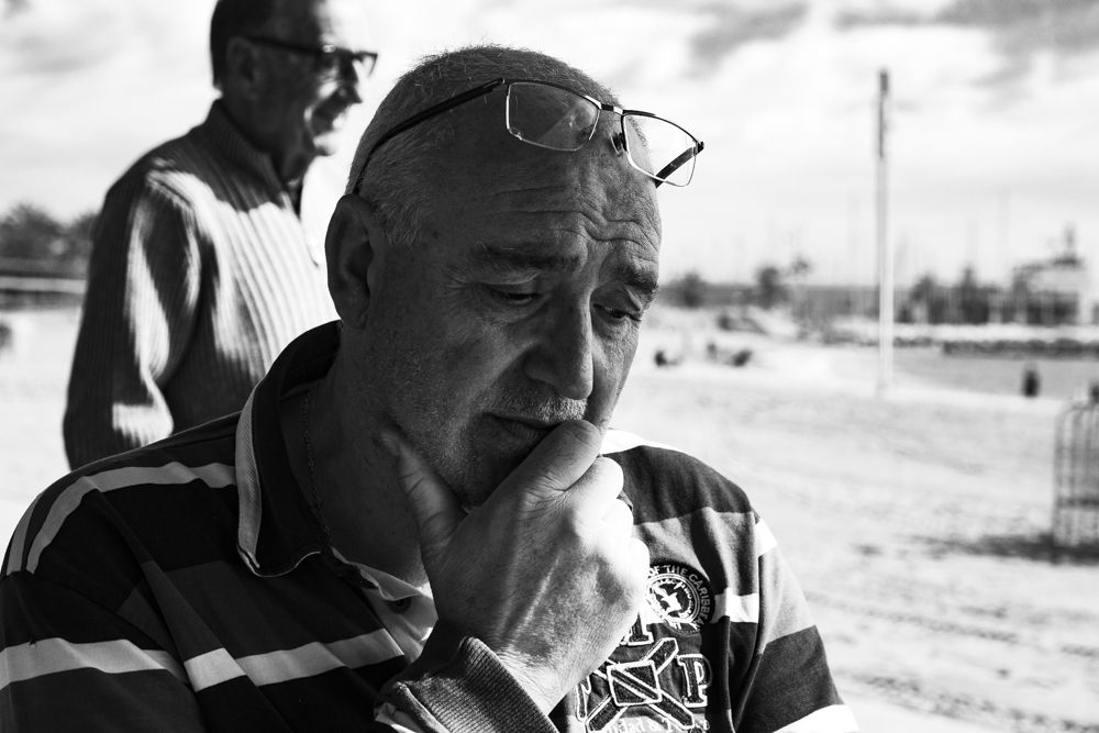 Hombre mayor pensativo con la mano en la barbilla durante una partida de dominó, en blanco y negro