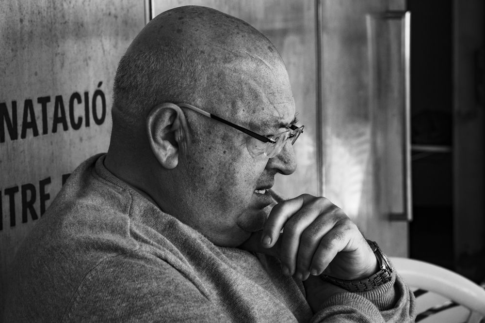 Hombre con gafas pensativo, con la mano en la boca, durante una partida de dominó, en blanco y negro