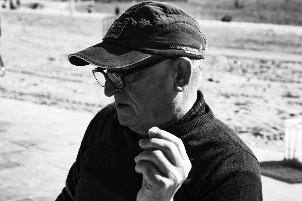 Hombre con gorra y gafas concentrado en la partida de dominó, en blanco y negro