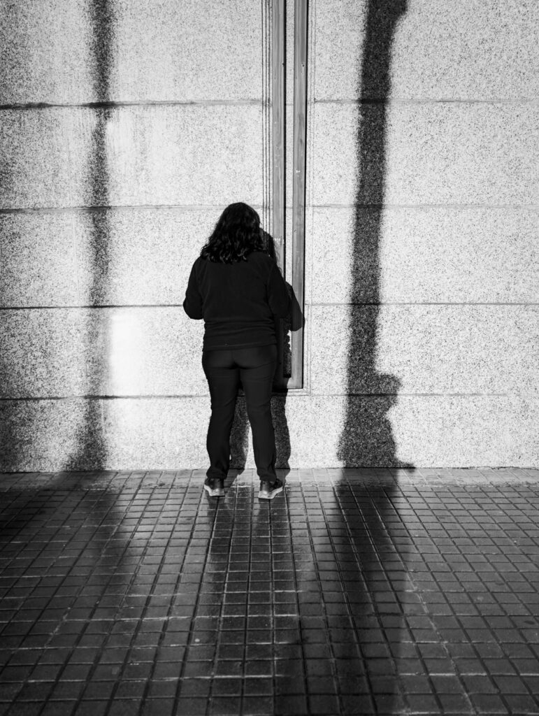 Mujer de espaldas frente a una pared con sombras alargadas, fotografía en blanco y negro hecha con móvil