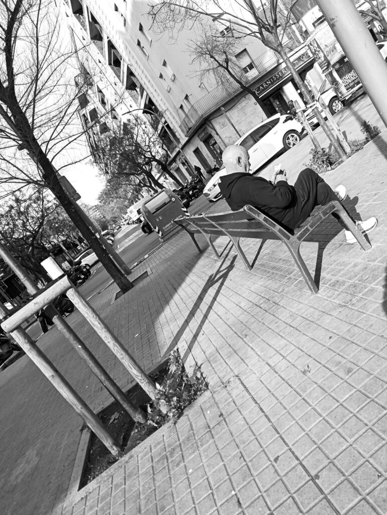 Hombre recostado en un banco de la calle, fotografía callejera en blanco y negro con encuadre inclinado