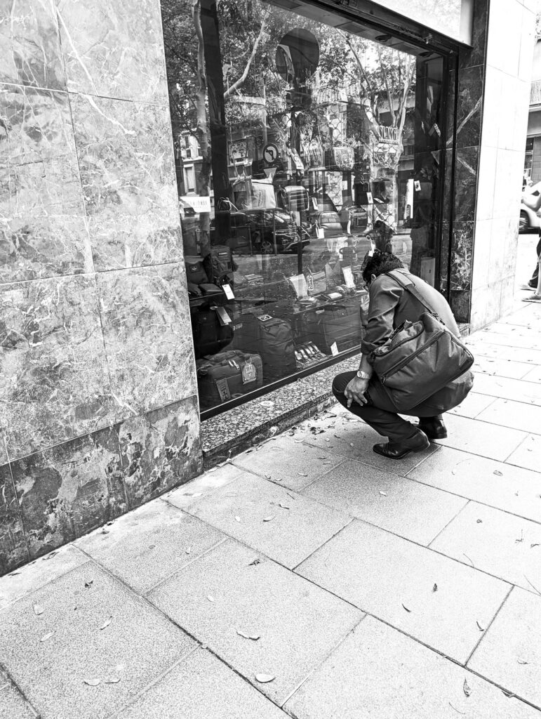 Hombre agachado mirando el escaparate de una tienda, fotografía de calle en blanco y negro hecha con smartphone