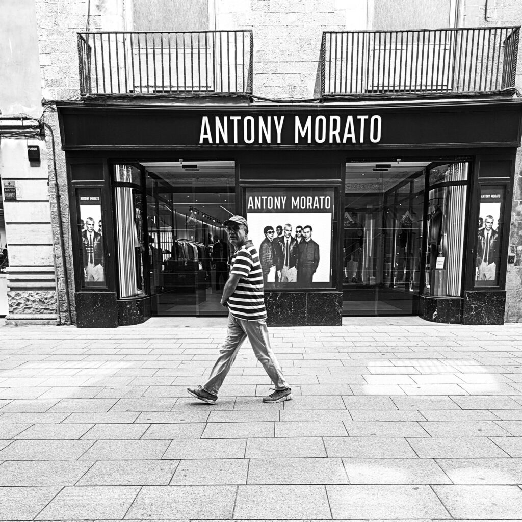 Hombre caminando solo frente a un escaparate en la calle, fotografía en blanco y negro
