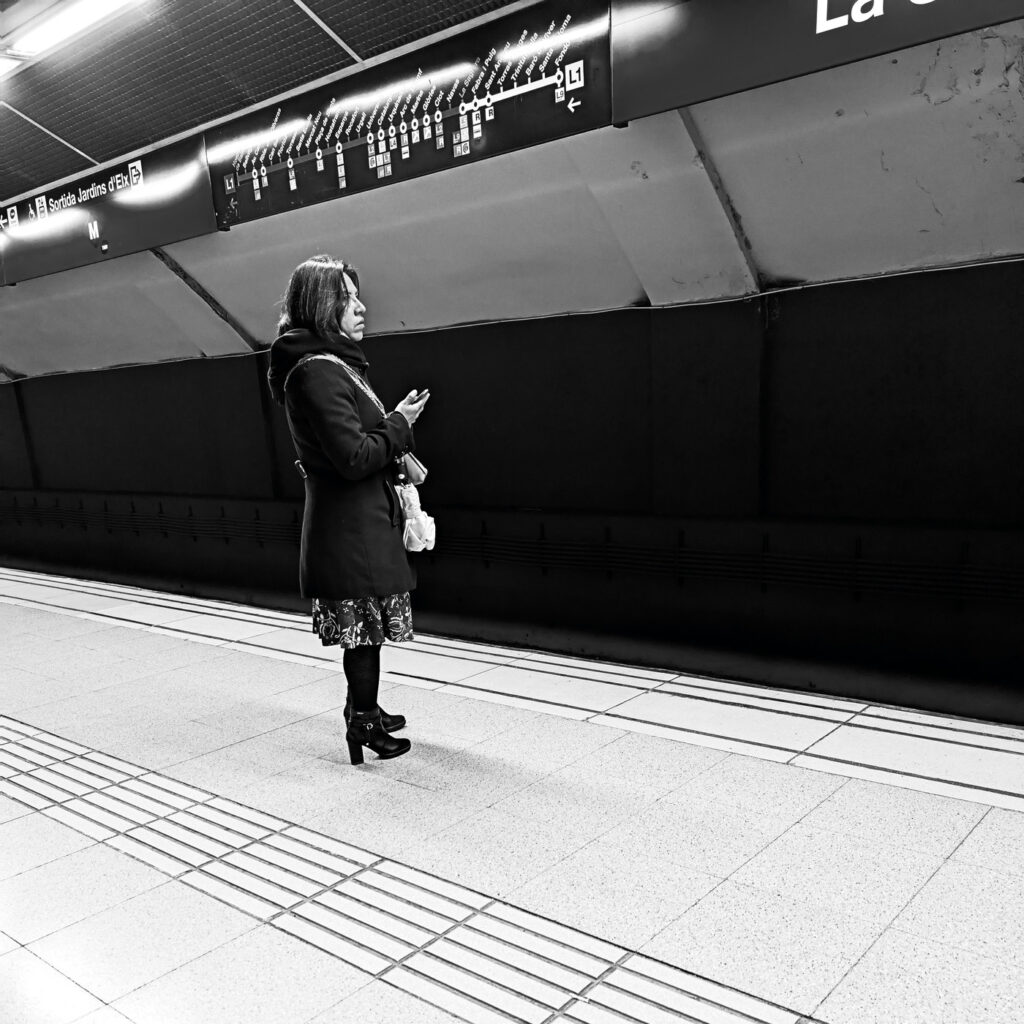 Mujer sola de pie en el andén del metro mirando al frente, fotografía en blanco y negro sobre la soledad
