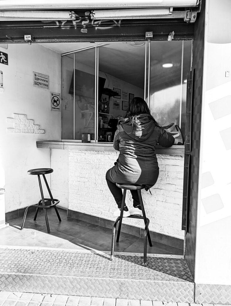 Mujer sentada en un taburete tomando café en la barra de un bar, fotografía de calle en blanco y negro